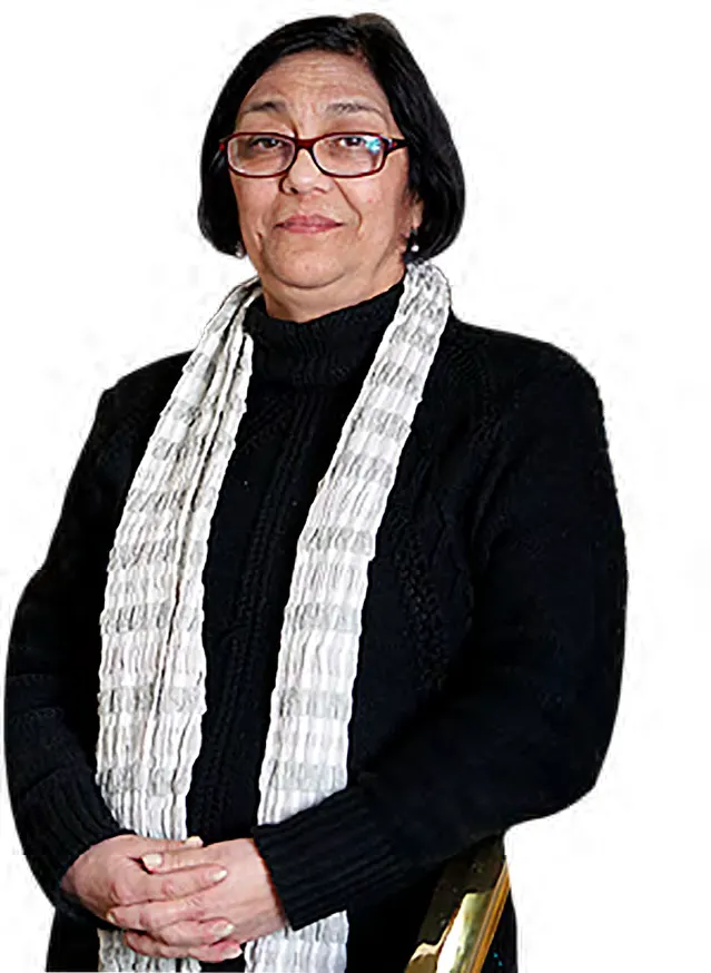 Retrato de Denisse Araya, con lentes y bufanda clara, de pie con las manos juntas.